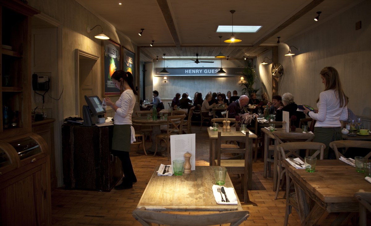 The Orange London restaurant dining room with wooden tables, pendant lighting, and patrons dining.
