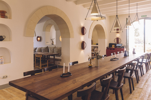 Dining room with long wooden table, chairs, arched white walls and pendant lights