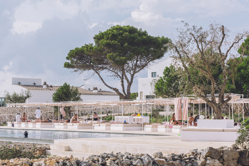Swimming pool area with white buildings and trees at Experimental Group's Menorca hotel