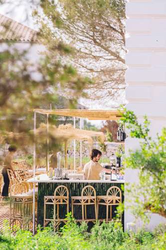 Outdoor terrace bar with green bar stools and bartender surrounded by lush vegetation