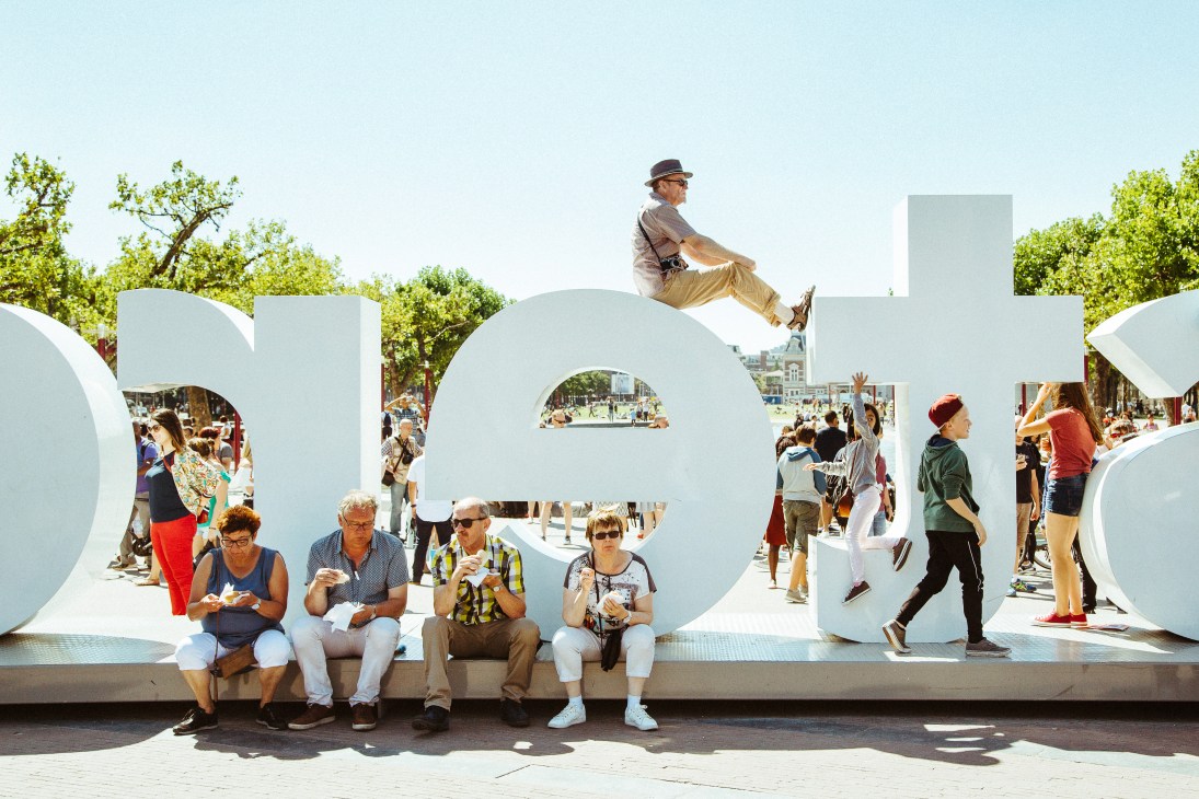 Tourists sitting and posing with the IAMsterdam sign outside the Rijksmuseum in Amsterdam.