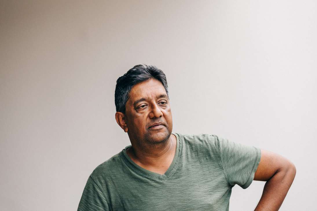Portrait of Prem Radhakishun, a political commentator, wearing a green v-neck shirt against a neutral background.