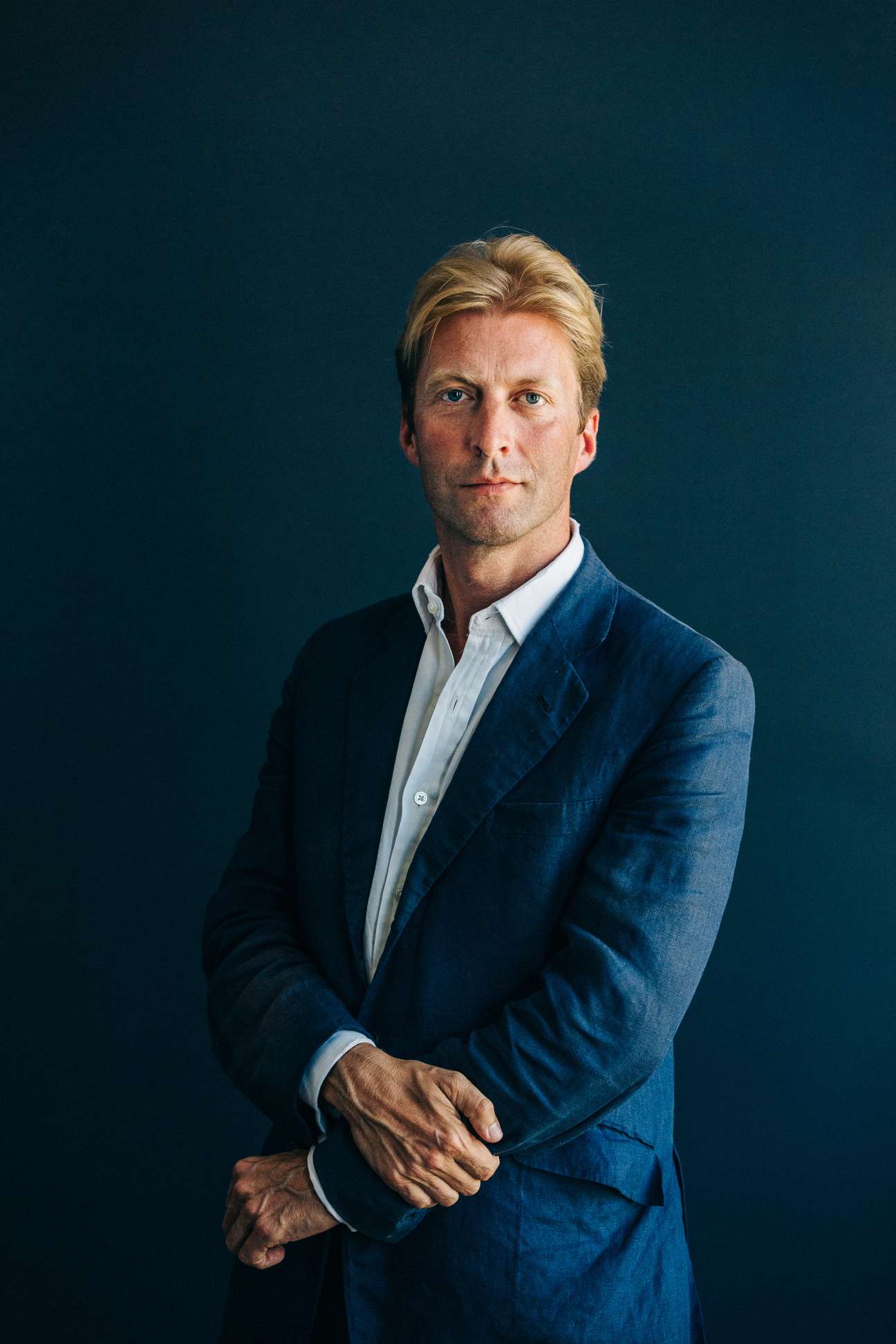 Taco Dibbits, director of the Rijksmuseum, in a portrait wearing a navy blazer against a teal background.