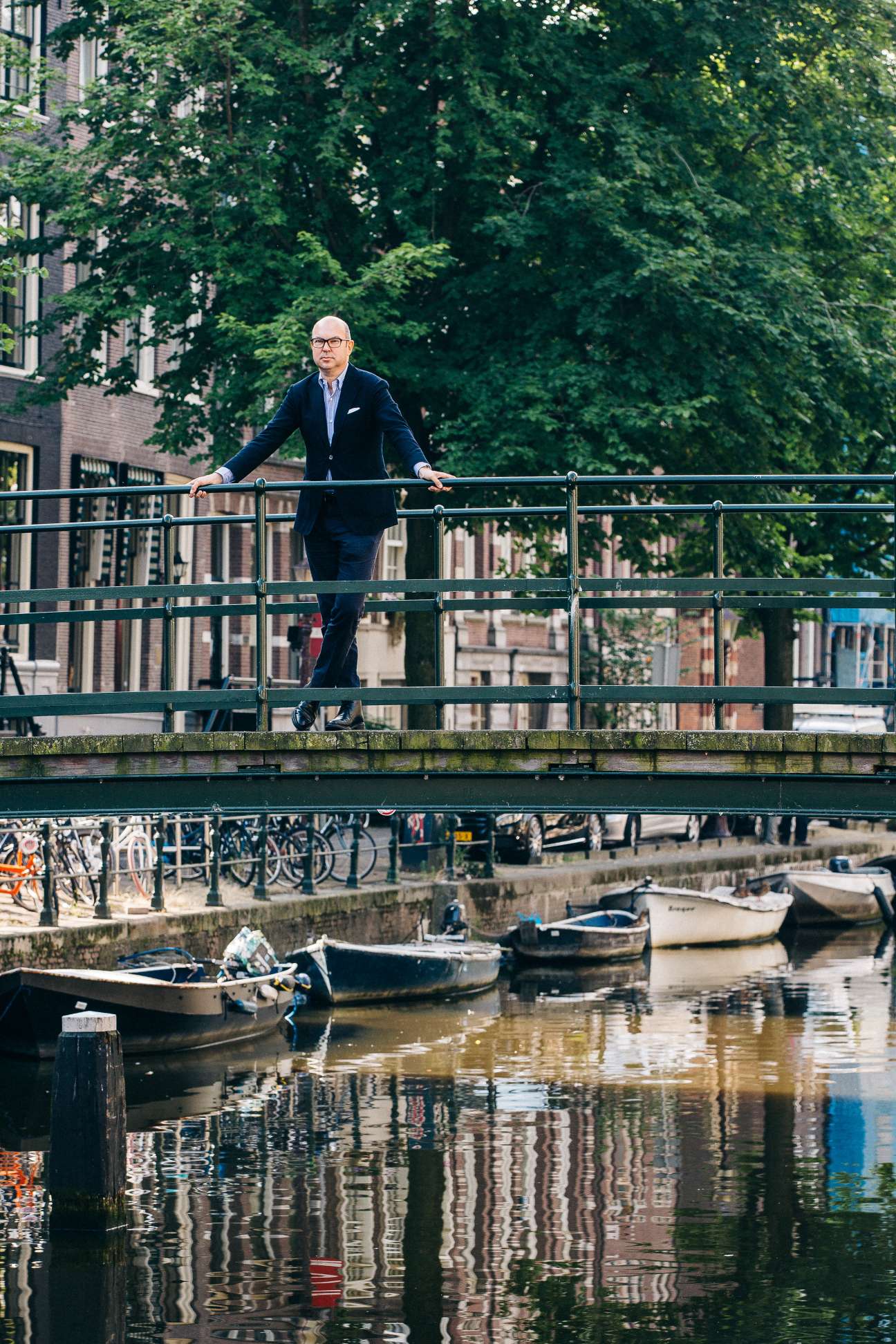 Guido van Nipsen, CEO of ANP, standing on a bridge over an Amsterdam canal with ivy-covered buildings behind him.