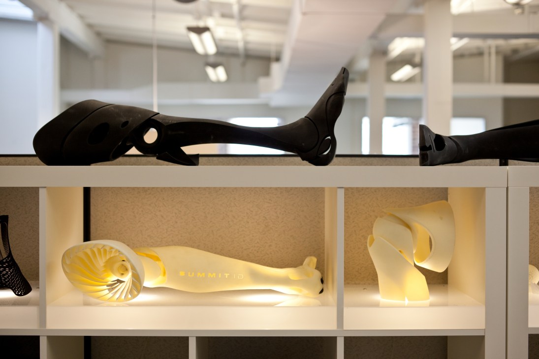 Black prosthetic limbs displayed on shelf above illuminated yellow prosthetic legs by Bespoke Innovations.