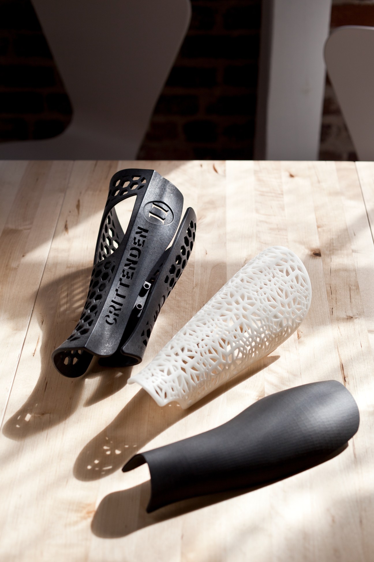Three 3D-printed prosthetic leg sleeves in black, white and gray with perforated patterns on wooden surface.