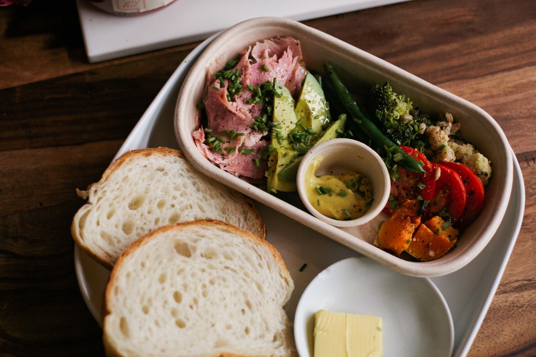 Sliced bread, cured meat with herbs, grilled vegetables and oil on a wooden table at Bread & Circus.