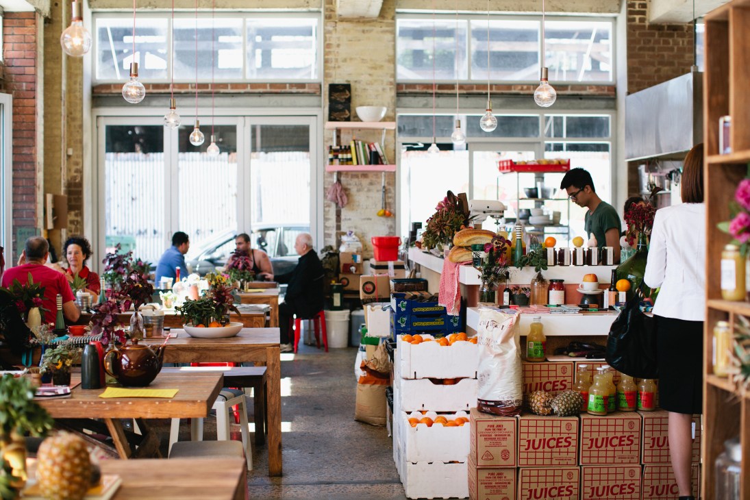 Bright warehouse café with wooden tables, pendant lights, fresh flowers, and customers dining while staff work behind counter at Bread & Circus.