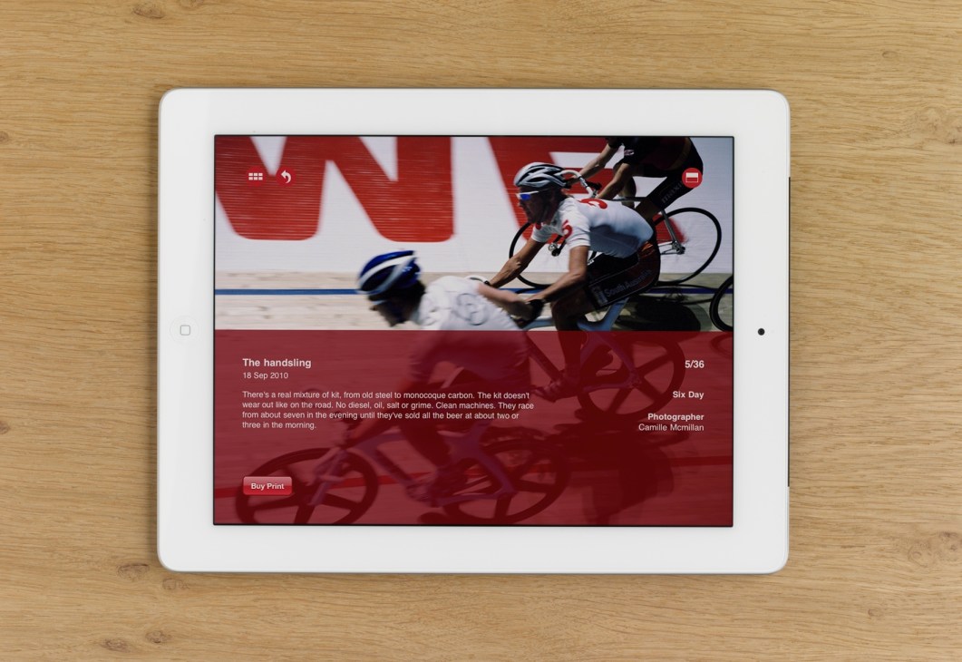 White iPad displaying The Collarbone app with cycling race photo and red interface on wooden surface.