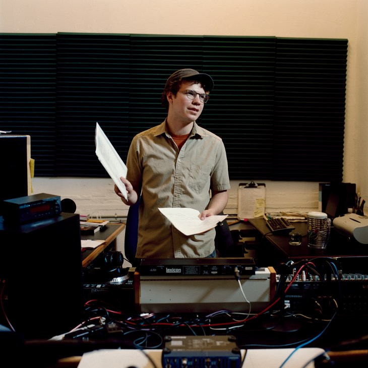 An AIR studio engineer holds papers while standing at a mixing console with audio equipment and wiring.