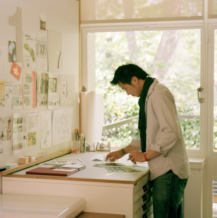 Person reviewing design materials at a desk with inspiration boards on the wall and garden visible through windows.