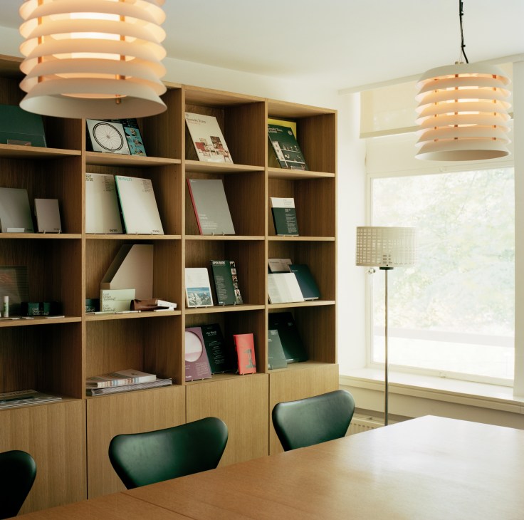 Winkreative meeting room with wood shelving, conference table, green chairs, and pendant lights.