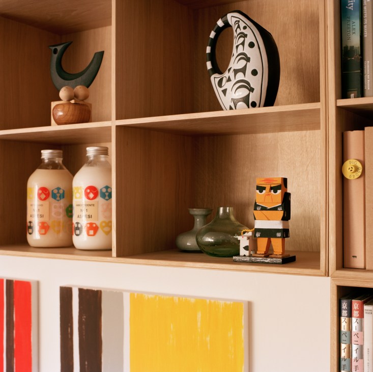 Wooden shelving unit displaying curated objects including sculpture, ceramic vessels, books, and decorative items.