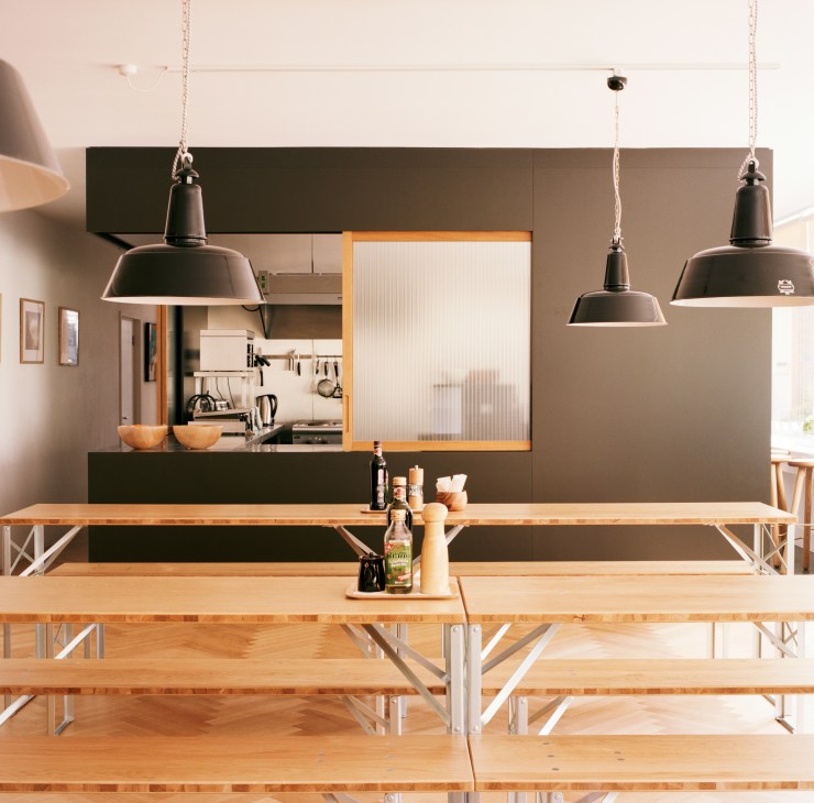 Modern industrial kitchen and dining space with oak tables, black pendant lights and open shelving designed by Andreas Martin-Löf.