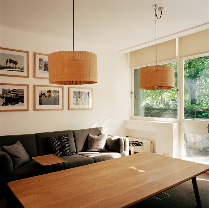 Modern meeting room with grey sofa, wooden table, framed photographs, and orange pendant lights overlooking gardens.