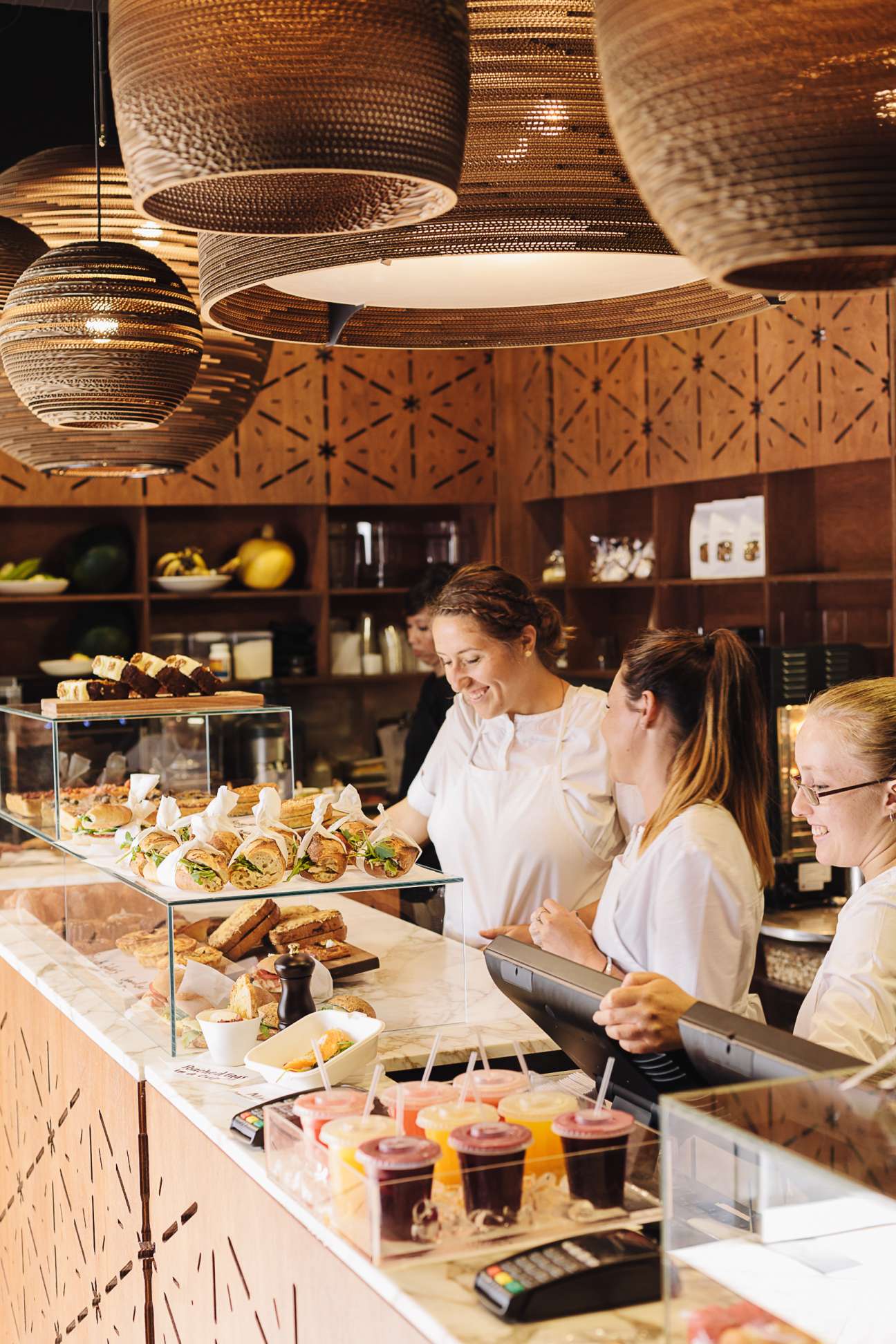 Three female staff members working behind a bakery counter with pastries and food displays.