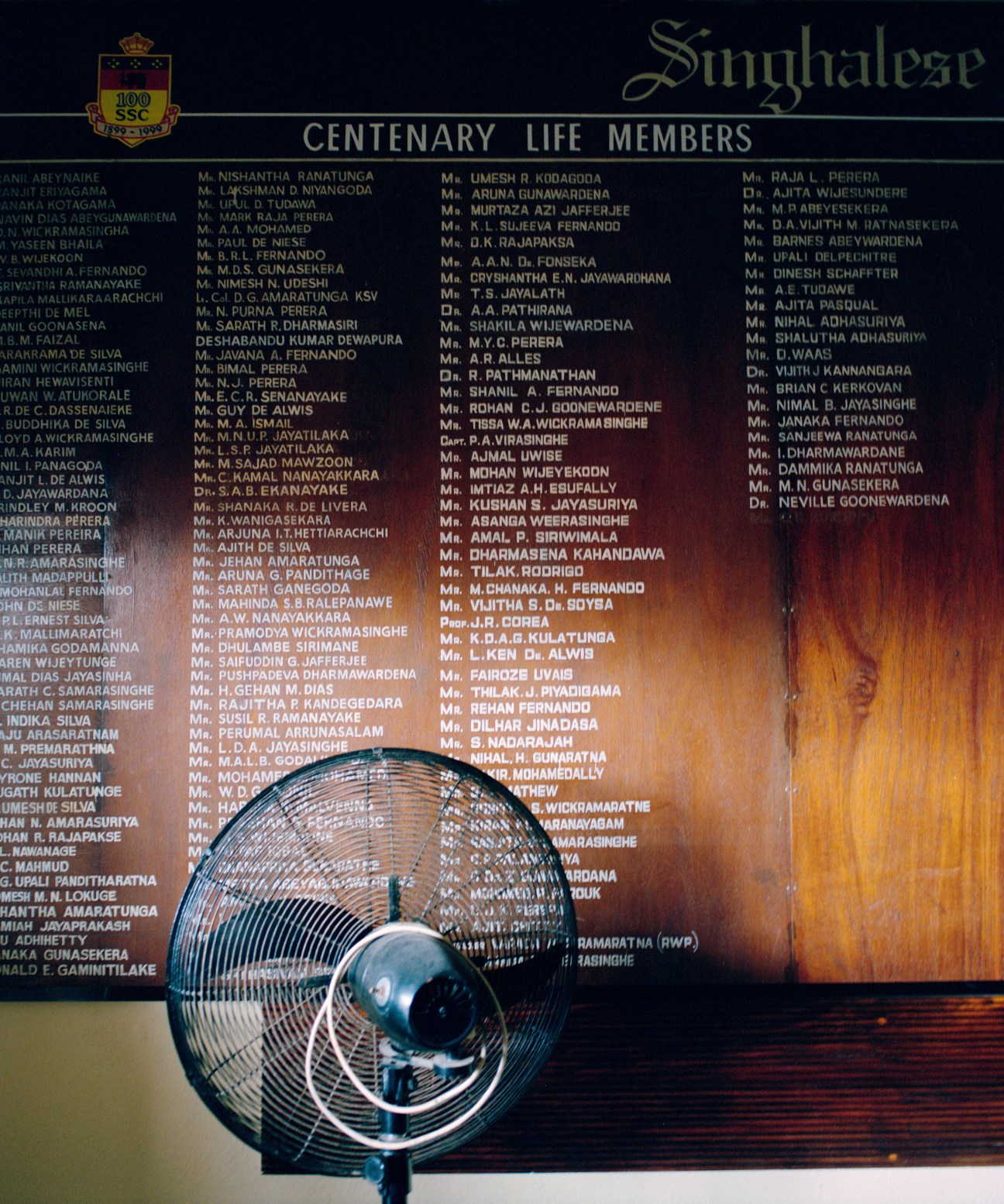 A vintage fan sits in front of a wooden plaque listing centenary life members at Broomfield Cricket Club.