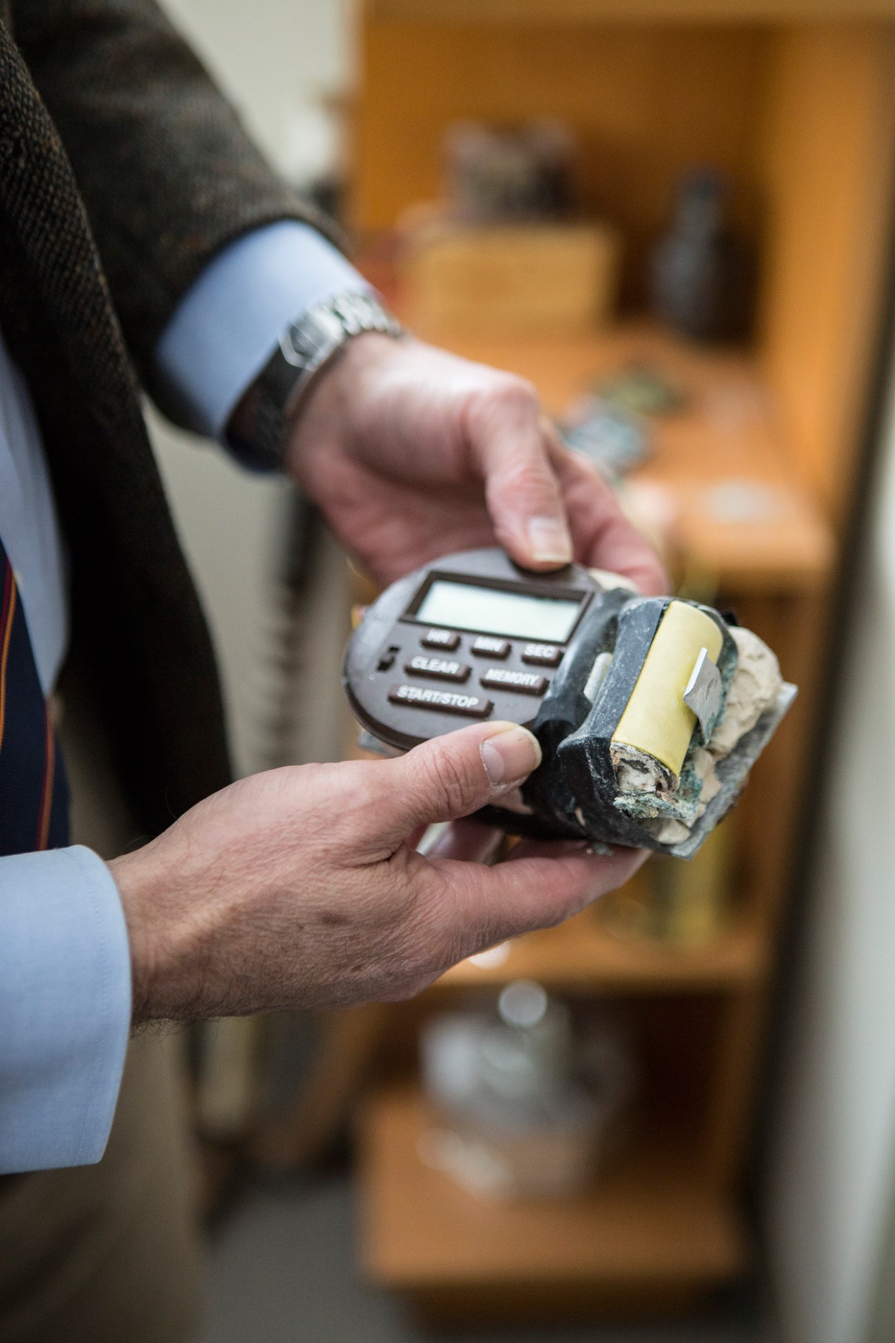 A person's hands holding a movie prop bomb from Die Hard, with a calculator visible in the background.