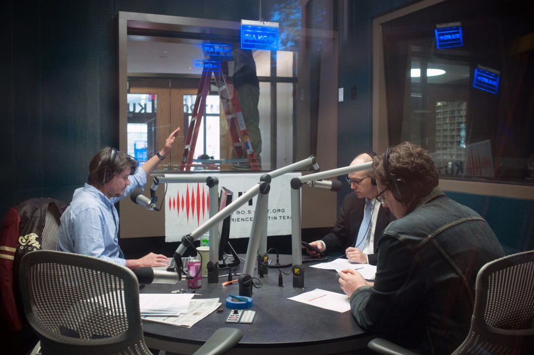 David Brown hosts Texas Standard news show at KUT radio station in Austin with production team in control room.