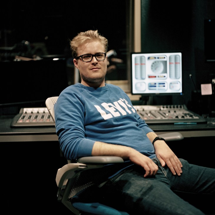 Texas Standard technical director Casey Cheek seated in a radio studio control room with audio equipment visible behind him.