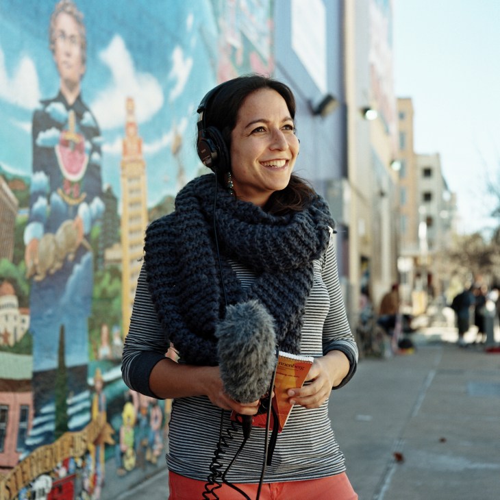 State politics reporter Veronica Zaragovia wearing headphones and holding a microphone outdoors against a colorful mural.