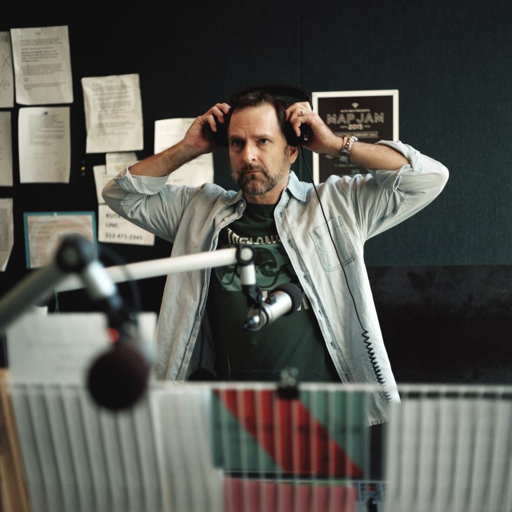 KUTX music host Rick McNulty adjusts headphones in his radio studio with microphone and equipment visible.