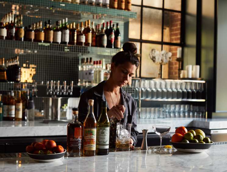 Bartender mixing cocktails at Firehouse Hotel bar with bottles on shelves behind.