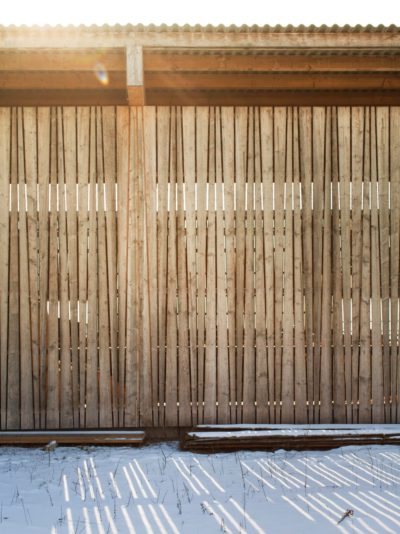 Wooden barn facade with slatted timber cladding and white painted sections in snowy landscape.