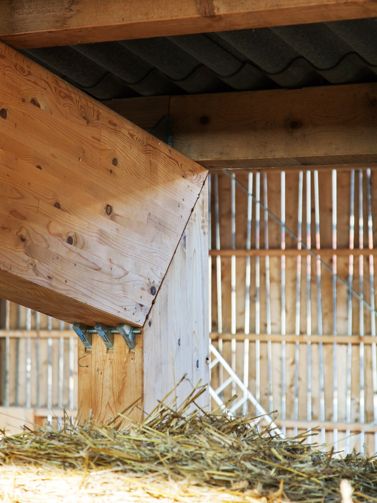 Close-up of wooden barn construction showing timber beams, slatted walls, and hay on the ground.