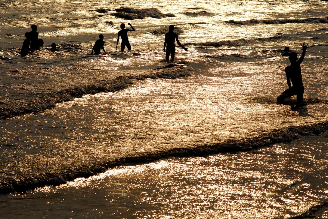 Silhouetted figures wading and swimming in Lake Tanganyika's golden waters at sunset.
