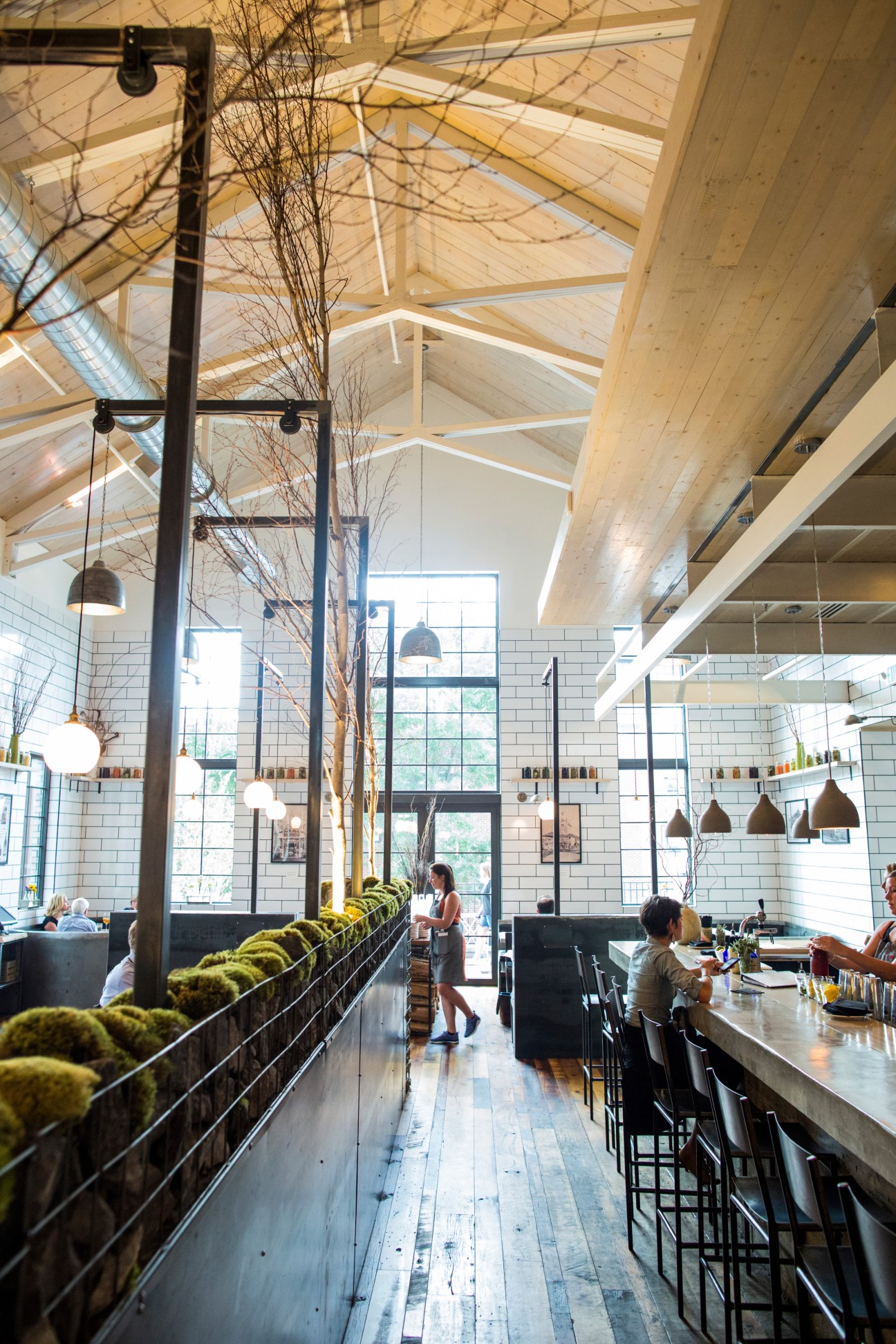 Interior of Butchertown Hall restaurant in Nashville with high ceilings, exposed wooden beams, white subway tile walls, and pendant lighting.
