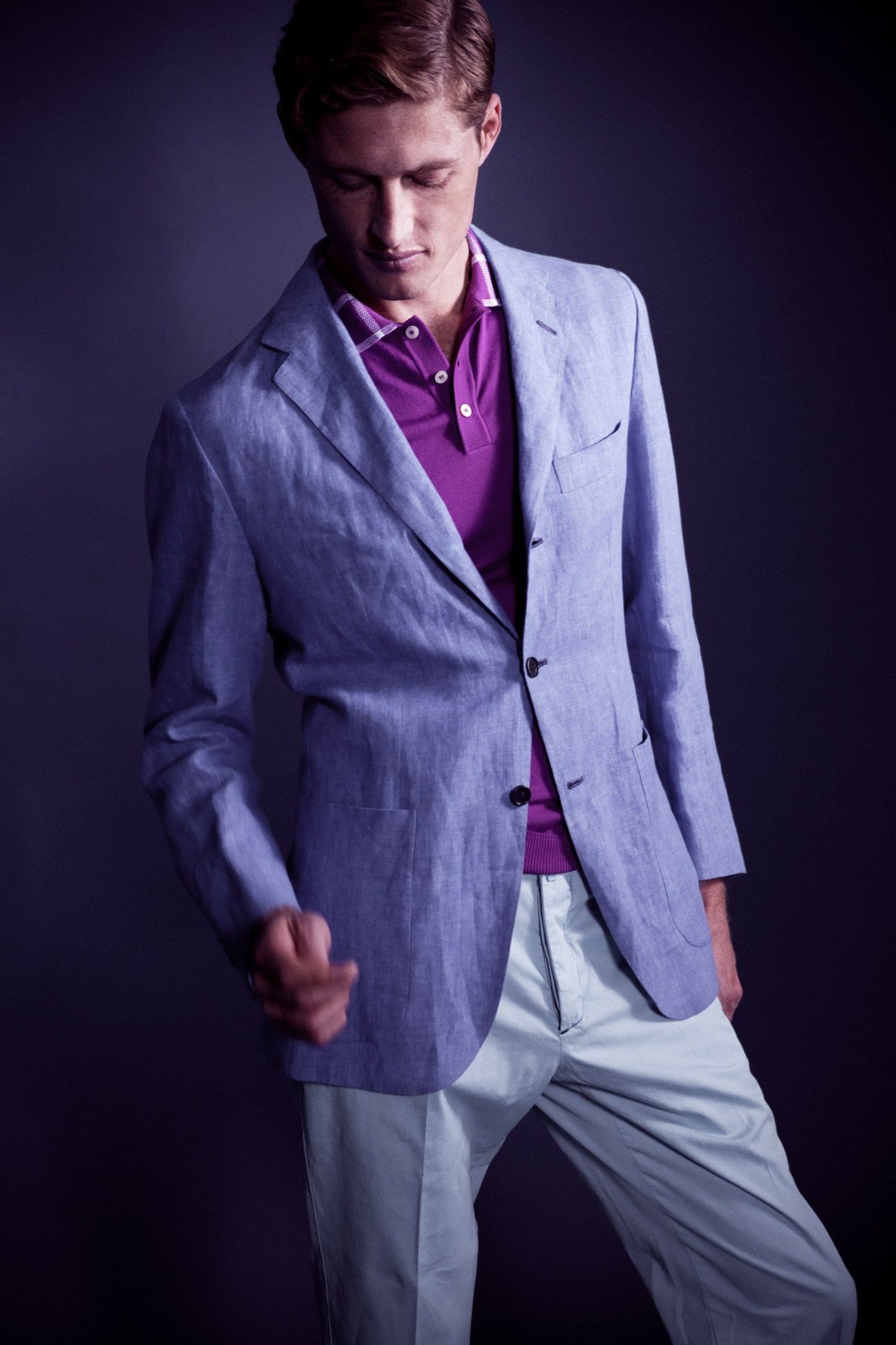 Man wearing a light blue Kiton blazer over a purple shirt and white trousers against a purple background.