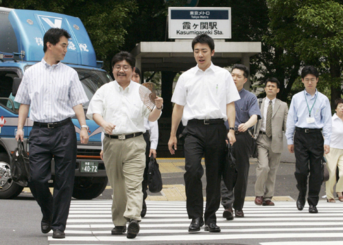 Japanese businessmen in white shirts and dark trousers crossing a street at a railway station during Cool Biz campaign.