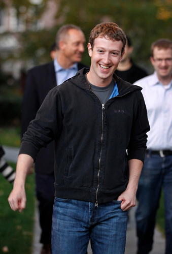 Man wearing black hoodie and jeans smiling at camera outdoors.