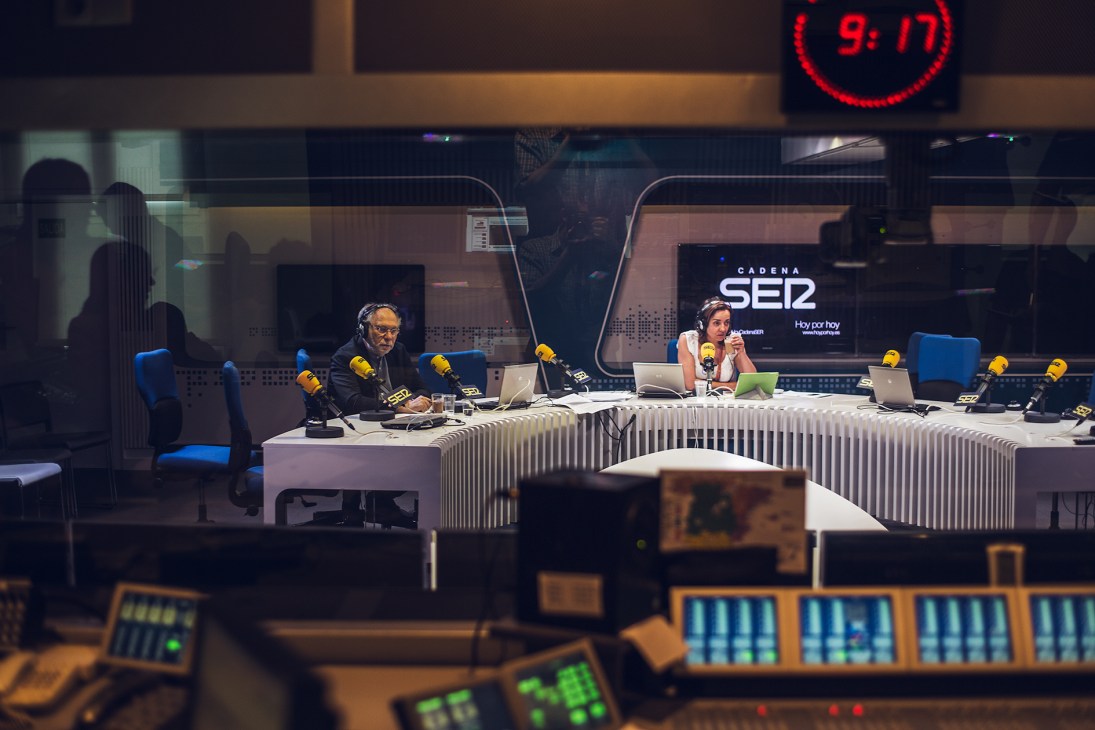 Pepa Bueno and a colleague broadcast at Cadena SER studio with microphones and laptops at a curved desk.