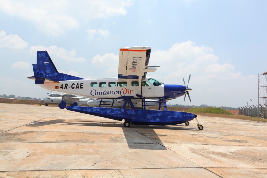 Cinnamon Air amphibian aircraft with floats parked on tarmac, featuring blue and white livery with registration 4R-CAE.
