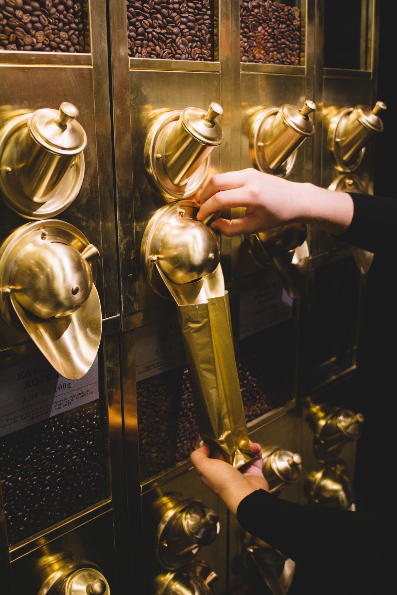 Hand reaching toward gold coffee bean dispensers displaying different roasts at Cafetino café.
