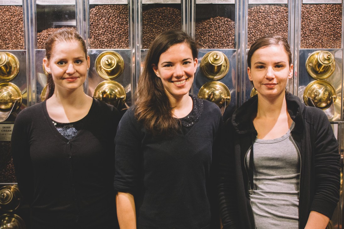 Three women smiling at Cafetino café, standing in front of gold coffee bean dispensers.