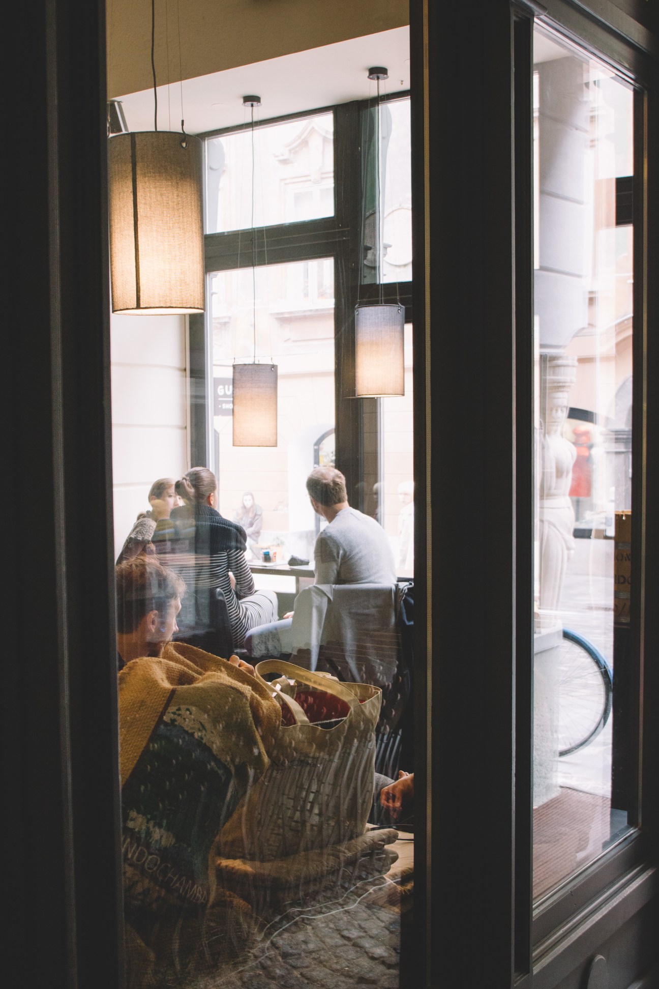 Customers seated at tables inside Cafetino café through large windows with pendant lighting.