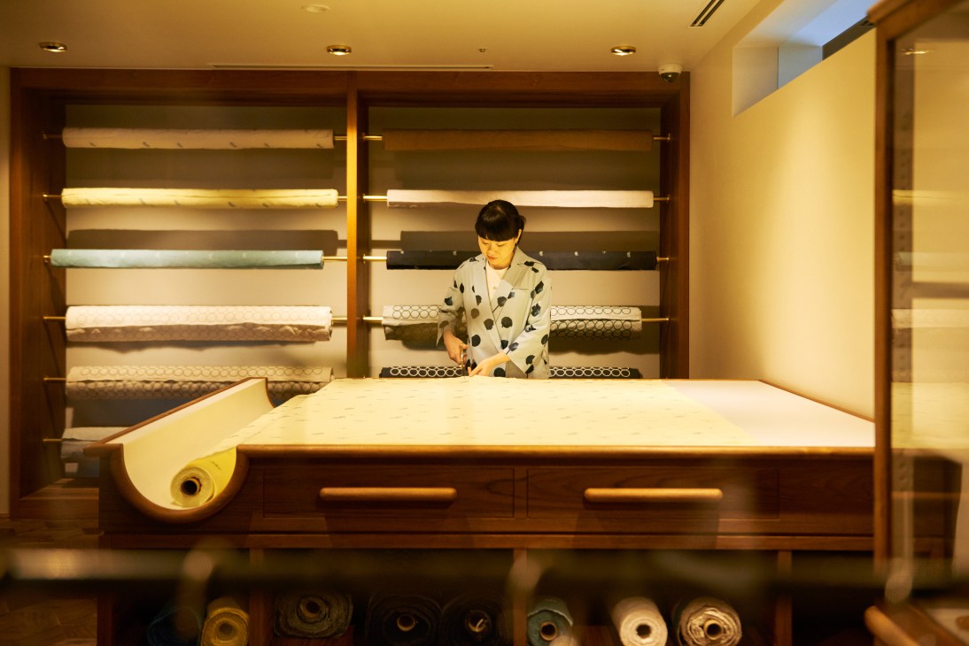 Woman selecting fabric rolls at Call shop display shelving in Tokyo.