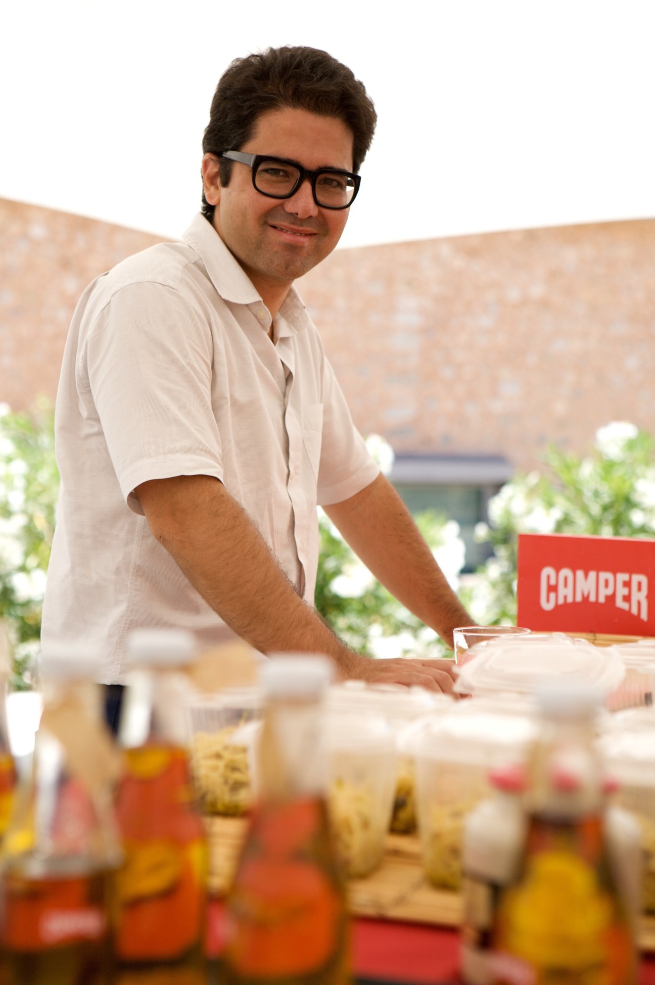Miguel Fluxa stands at an outdoor lunch table with food and a red Camper sign visible behind him.