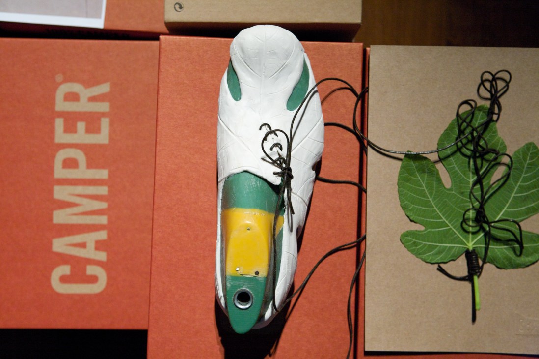 A deconstructable Camper shoe prototype in white, green and yellow displayed on branded packaging.