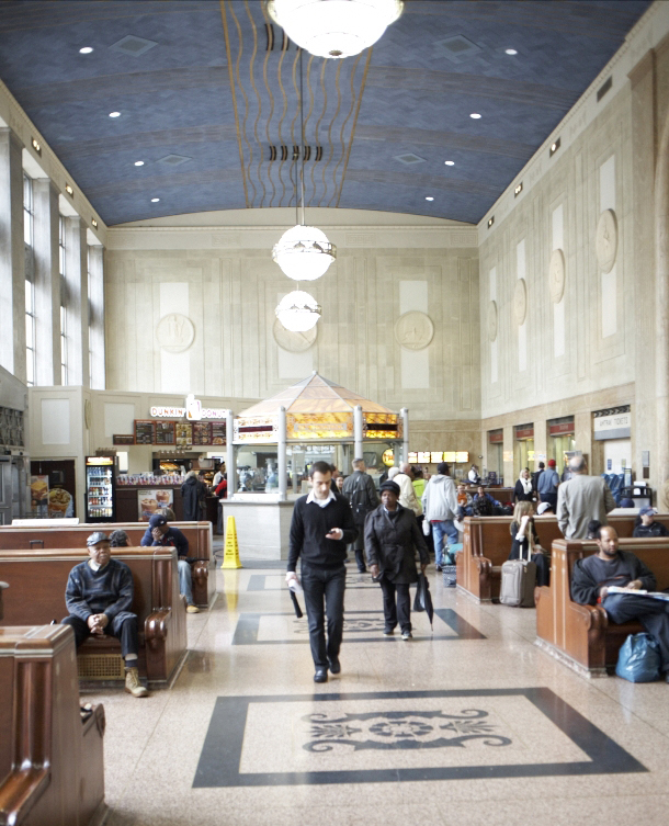 Interior of Newark's Penn Station showing ticket counters, pendant lighting, and passengers in the main hall.