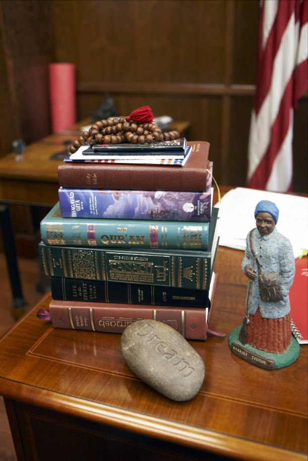 Stack of religious texts including Bible, Torah, Quran and Bhagavad Gita on wooden desk with decorative items.