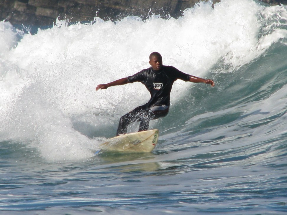 Young Black surfer riding a wave on a yellow surfboard off the coast of South Africa.