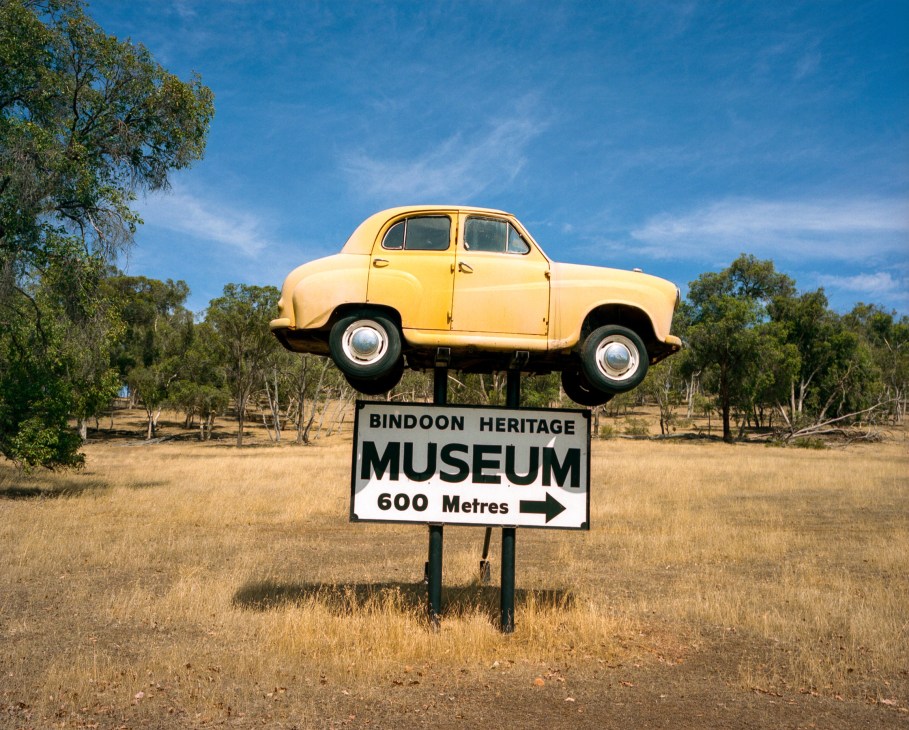 Yellow vintage car mounted on a sign for Bindoon Heritage Museum along Australian highway