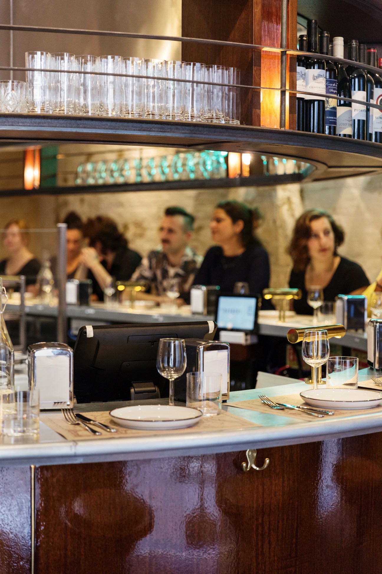 The Barbary restaurant counter with place settings, wine bottles on shelves above, and diners seated in the background.