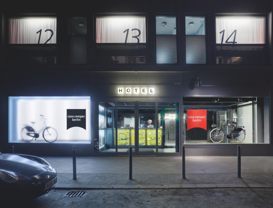 CasaCamper Berlin hotel storefront at night with numbered windows and bicycle displays.