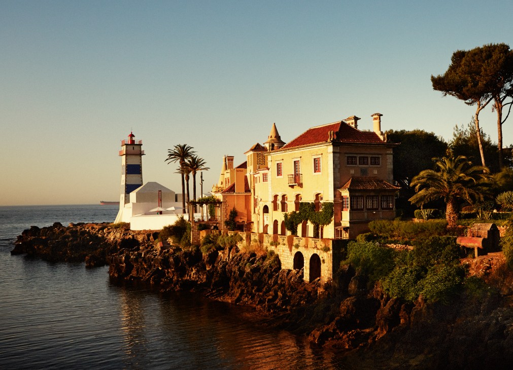 Casa de Santa Maria palatial residence with attached lighthouse overlooking rocky Cascais coastline at sunset.