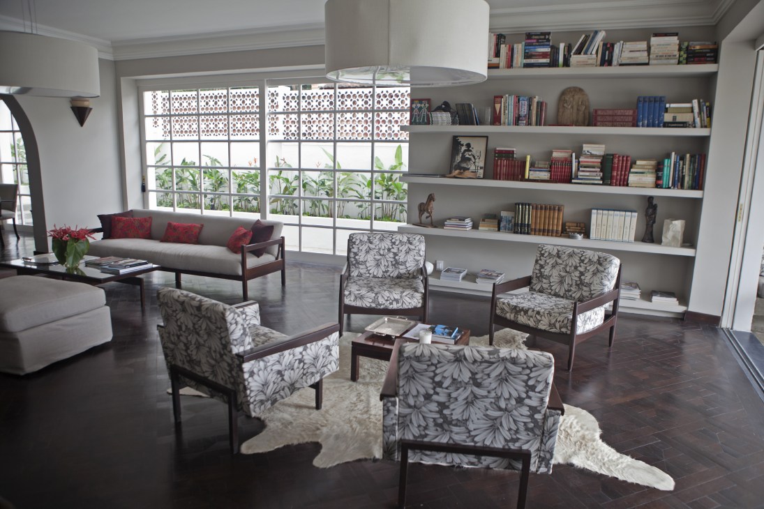 Modern living room with bookshelves, mid-century furniture, and large windows with decorative screens.